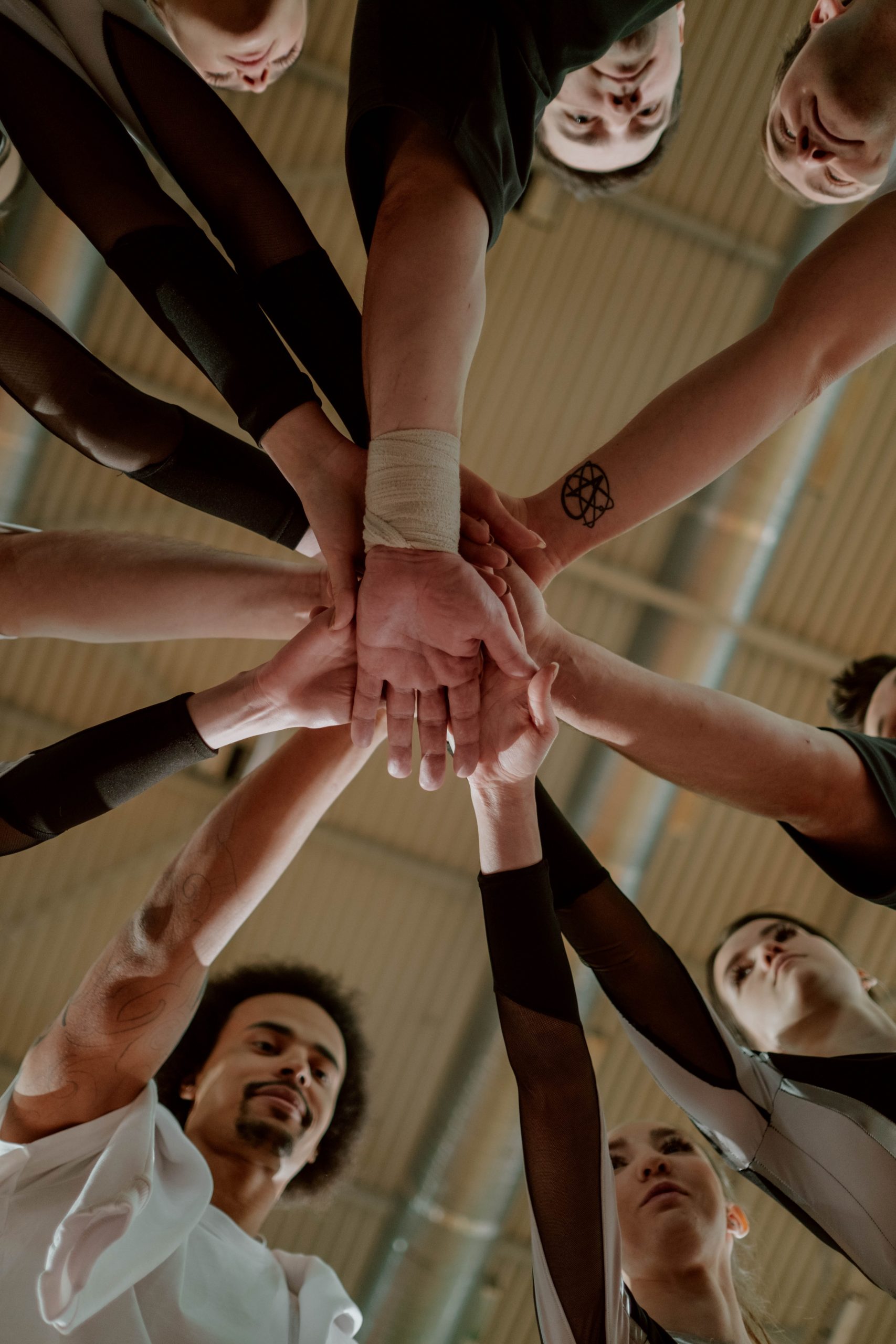 A circle of people who hold one hand stacked in the middle of the circle, taken from the ground upwards.